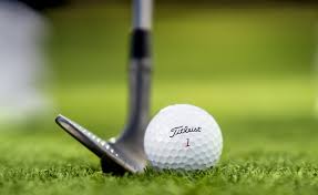 A white Titleist golf ball about to be struck by a wedge on the fairway 